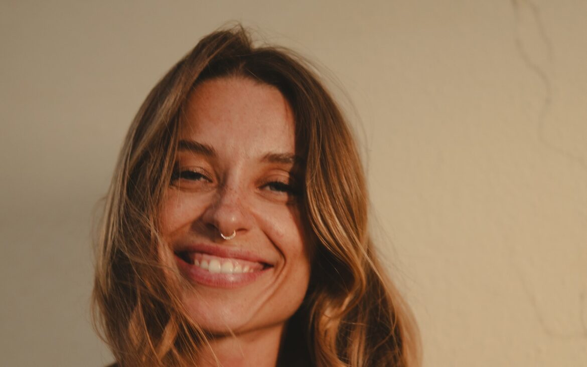 Kate Zubok smiling in an artist-supplied portrait against a warm neutral background.