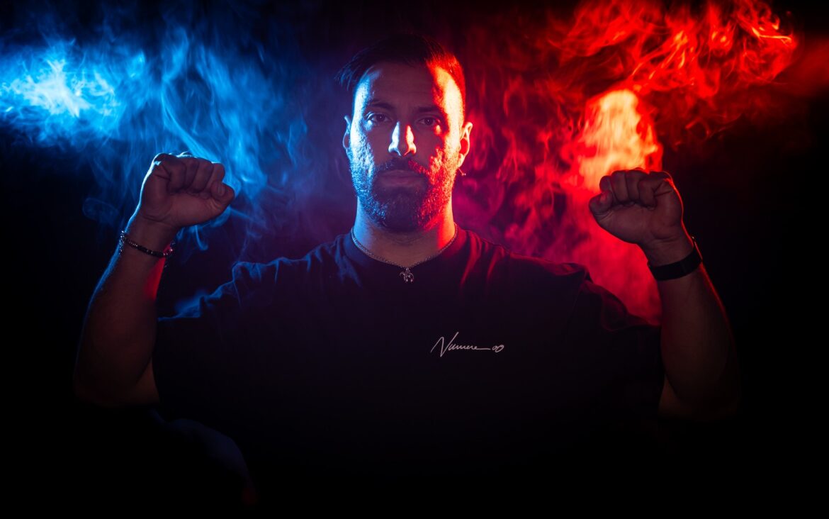 Massimo Conte in a blue-and-red-lit portrait with his fists raised.
